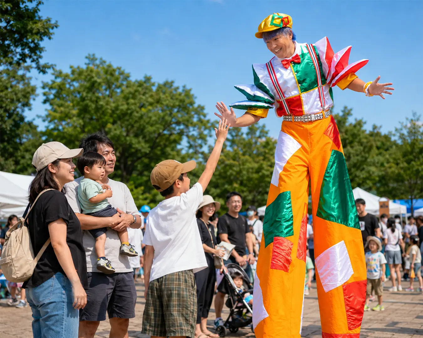スティルトを装着したパフォーマーがイベント会場で来場者と交流するグリーティングの様子
